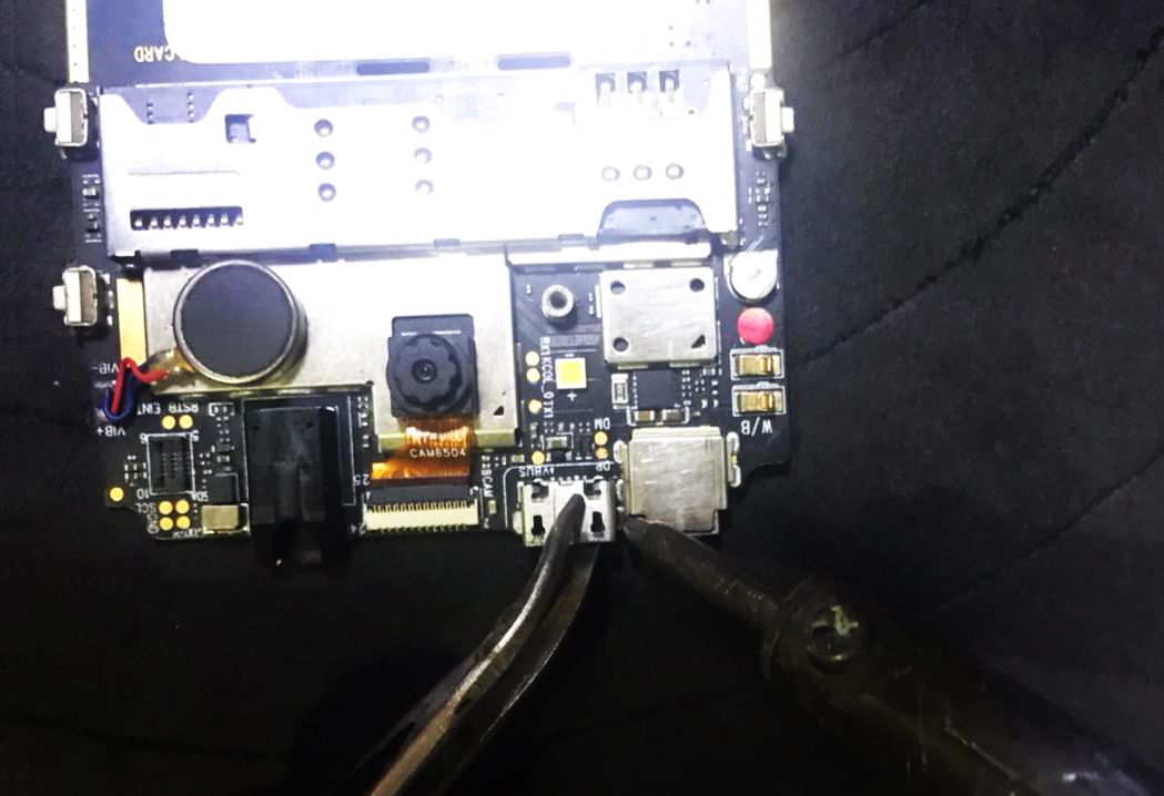 Using a soldering gun and tweezers to remove the charging port of the phone